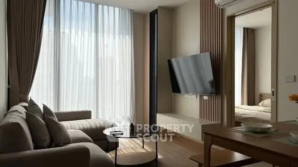 Modern living room with large windows and stylish decor, leading to a cozy bedroom.