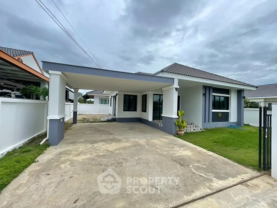 Modern single-story house with spacious driveway and lush green lawn under cloudy sky.