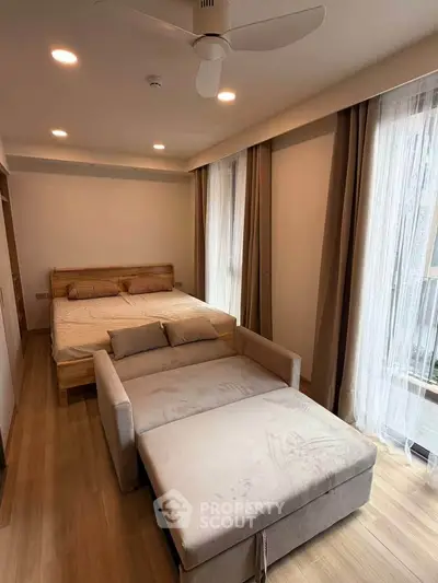 Modern bedroom with cozy bed and sofa, wooden flooring, and large windows with curtains.