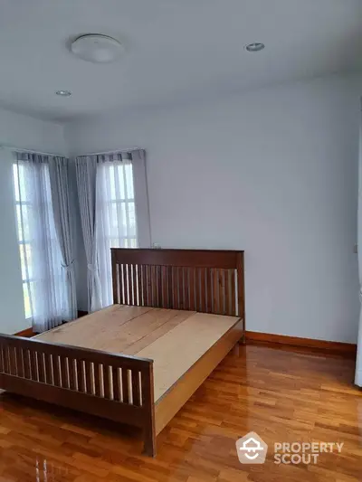 Spacious bedroom with wooden bed frame and large windows, offering ample natural light.