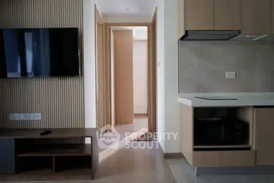 Modern apartment interior with sleek kitchen and cozy living area, featuring a wall-mounted TV and stylish cabinetry.