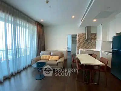 Modern open-layout living room with kitchen, featuring sleek furniture and large windows for natural light.