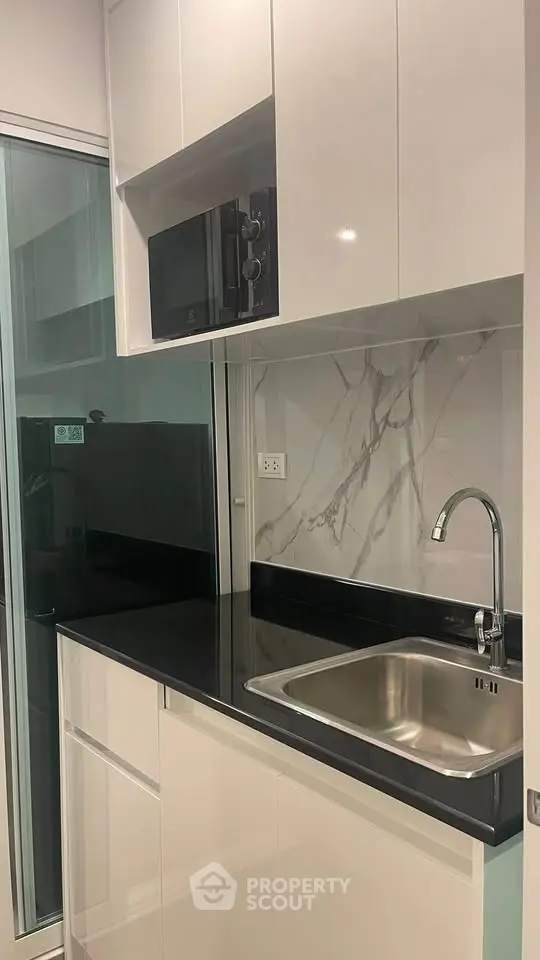 Modern kitchen with sleek cabinetry, black countertop, and built-in microwave in a compact layout.