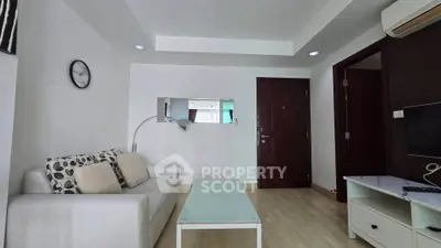 Modern living room with white sofa, glass coffee table, and wall-mounted TV in a stylish apartment.