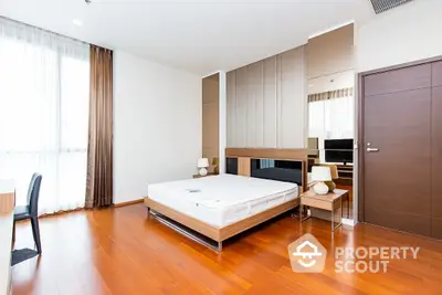 Spacious bedroom with polished hardwood floors, modern furniture, and ample natural light streaming through large windows, creating a warm and inviting atmosphere.