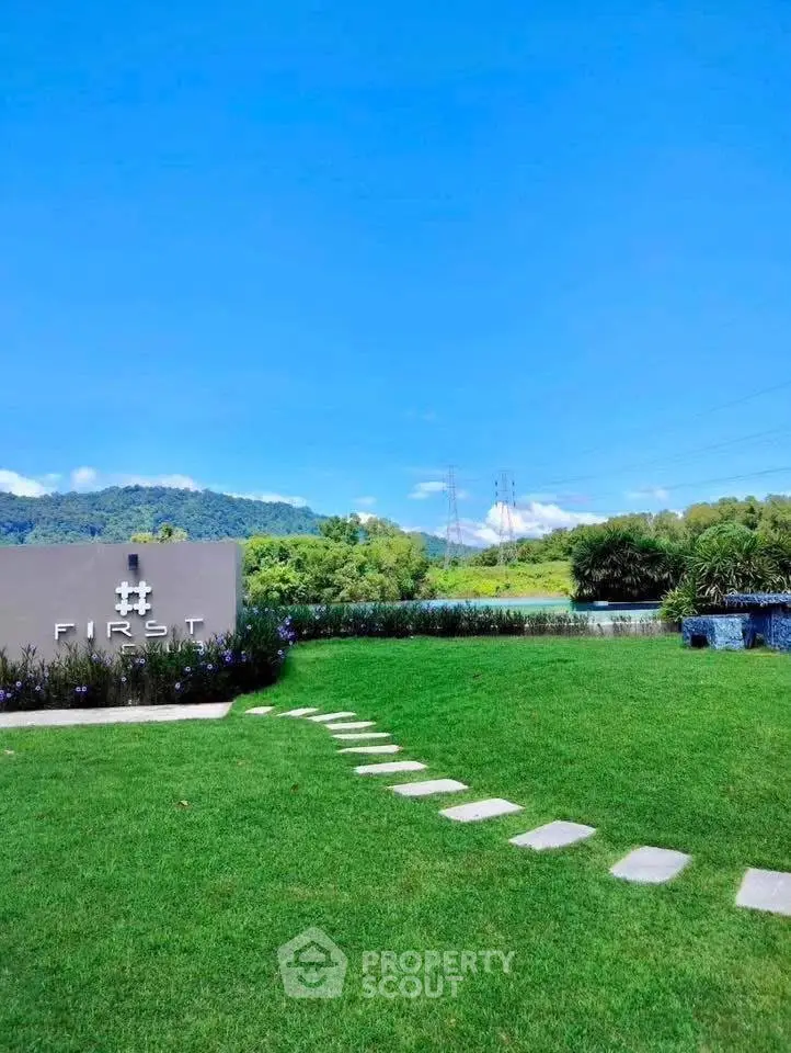 Scenic view of lush green garden with stepping stones and distant hills under clear blue sky.