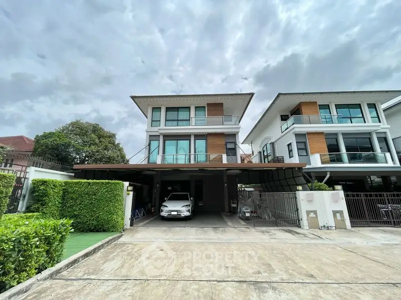 Modern two-story house with carport and lush greenery in a suburban neighborhood.