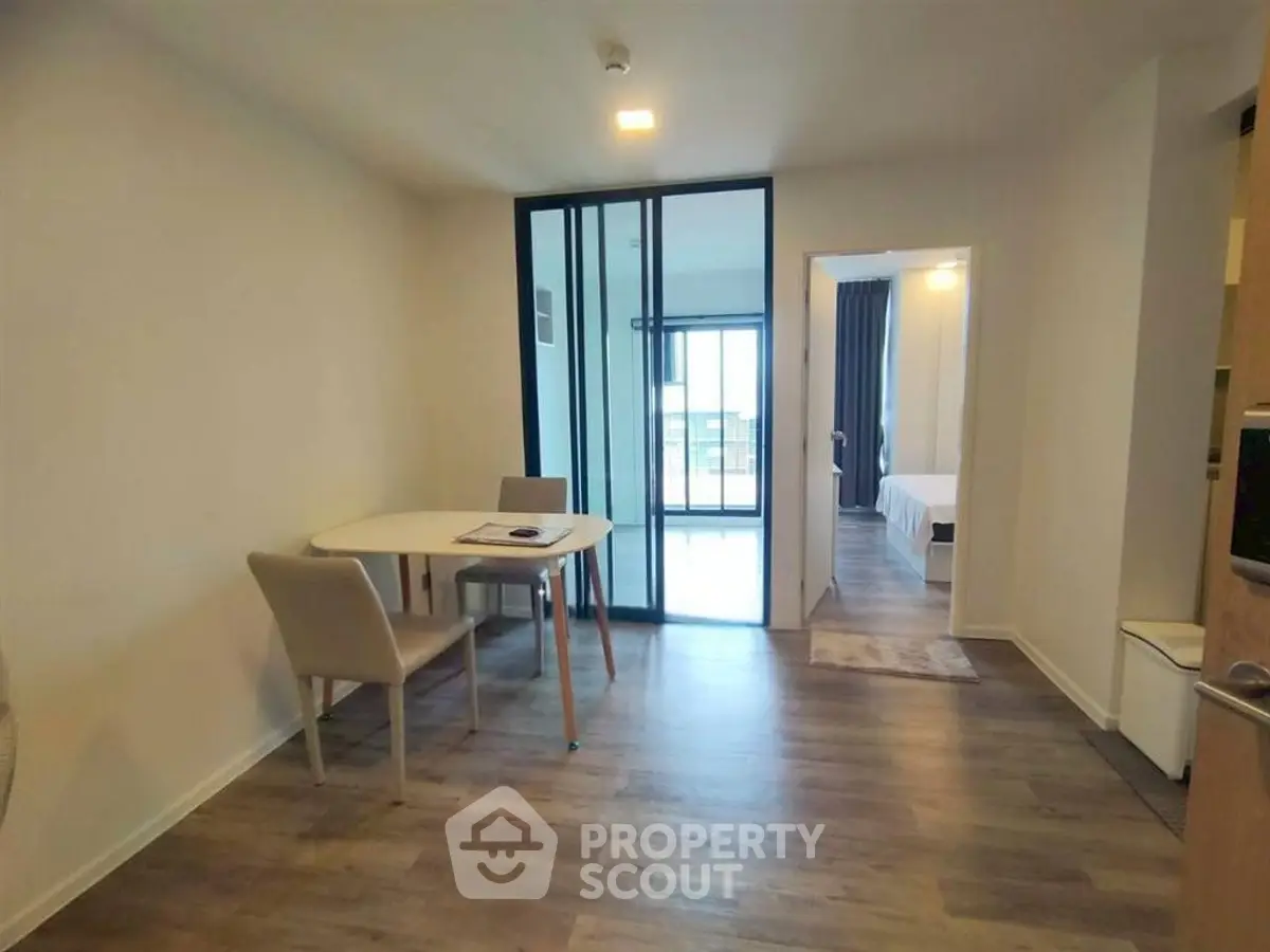 Modern apartment interior with dining area and view into bedroom, featuring sleek design and natural light.