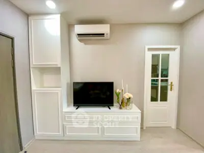 Modern minimalist living room with sleek white entertainment unit, wall-mounted air conditioner, and elegant French doors leading to another room.