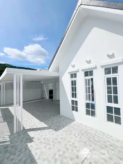 Sunlit spacious patio of a modern white villa with elegant French windows and a serene mountain backdrop, perfect for upscale living.