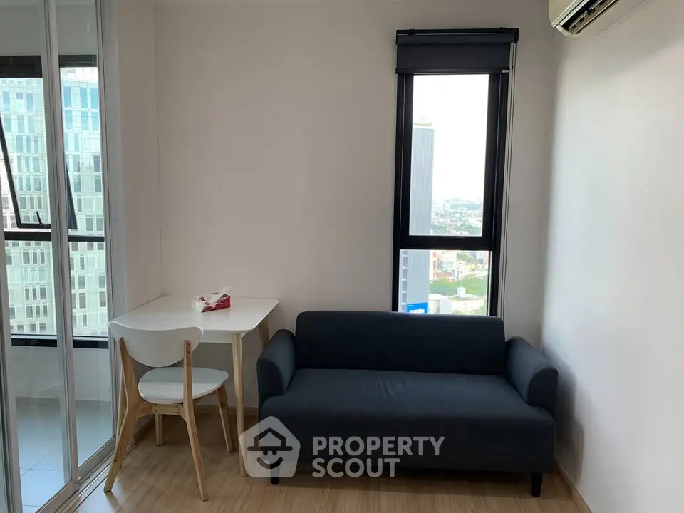 Cozy modern living area with compact sofa and dining table, featuring city view.