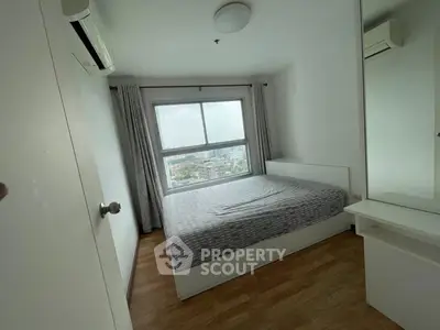 Cozy bedroom with large window offering city views, featuring modern furnishings and air conditioning.
