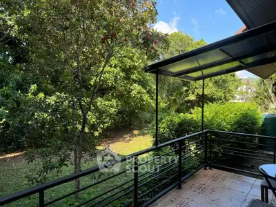 Charming garden view from a cozy balcony with lush greenery and clear blue sky.
