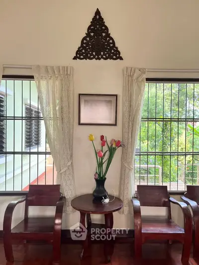 Charming living room with wooden chairs, decorative wall art, and a vase of tulips by large windows.