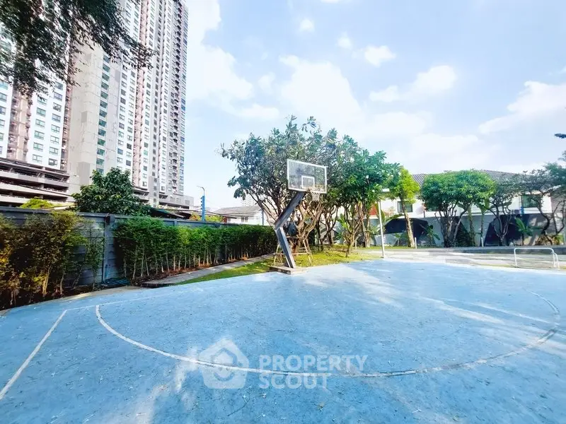 Spacious outdoor basketball court in modern residential complex with lush greenery and high-rise buildings.