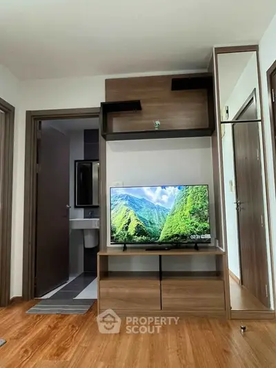 Modern living room with sleek wooden TV stand and wall-mounted shelves, adjacent to a bathroom entrance.