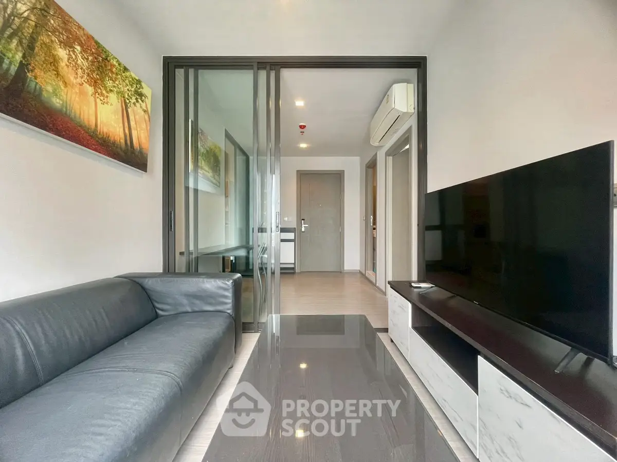 Modern living room with sleek black sofa, large TV, and glass partition in stylish apartment.