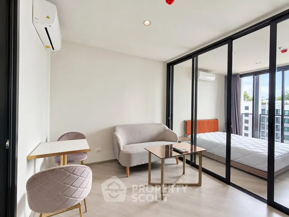 Modern studio apartment with glass partition, cozy seating, and natural light.