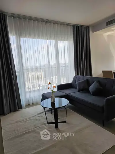 Modern living room with elegant sofa and floor-to-ceiling windows offering natural light and a serene view.