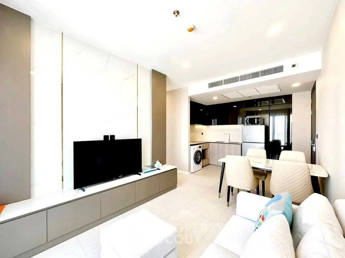 Modern living room with open kitchen, featuring sleek furniture and appliances.