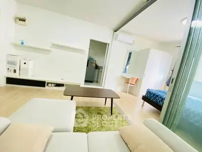 Modern open-plan living room with cozy seating and adjacent bedroom in stylish apartment.