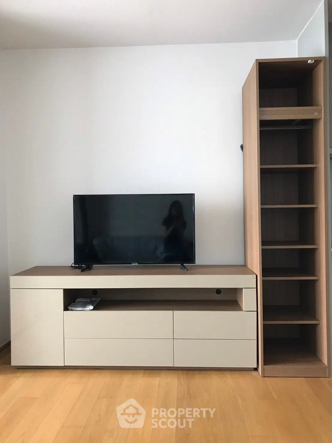 Modern living room with sleek TV stand and wooden shelving unit on polished hardwood floor.