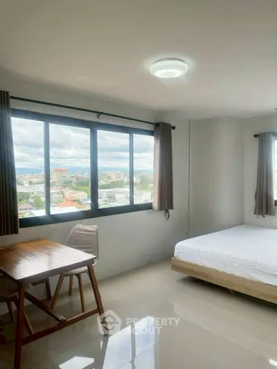 Bright bedroom with large windows offering stunning city views, featuring a cozy bed and a stylish wooden desk.