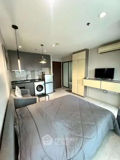 Modern studio apartment with cozy bed, washing machine, and sleek kitchen area.