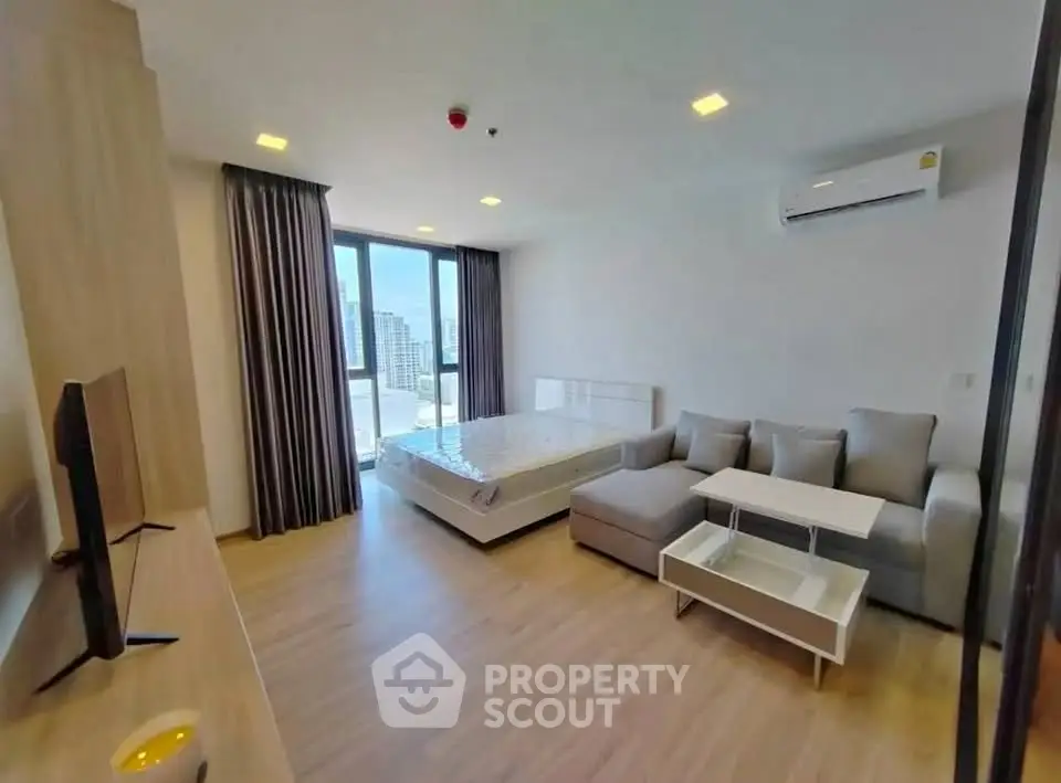 Modern studio apartment with stylish furniture and city view, featuring a cozy living area and large windows.