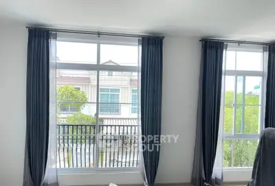 Bright living room with large windows and elegant curtains overlooking a suburban neighborhood.