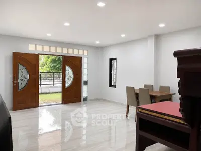 Spacious living room with elegant wooden doors and dining area, featuring modern lighting and a serene garden view.