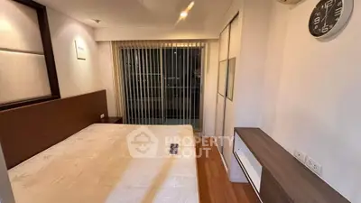 Modern bedroom with wooden flooring and large window with vertical blinds.