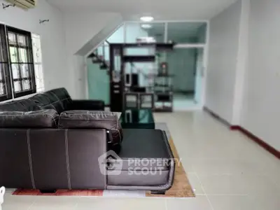 Spacious living room with modern black leather sectional sofa and sleek tile flooring.