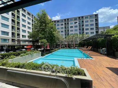Modern apartment complex with a pristine swimming pool and lush greenery under a clear blue sky.