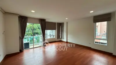 Spacious empty living room with hardwood floors and large windows opening to a balcony.