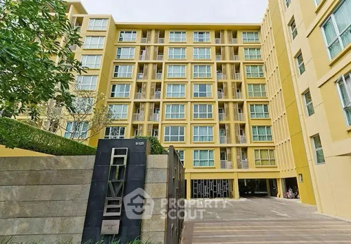 Modern yellow apartment building exterior with lush greenery and spacious entrance.