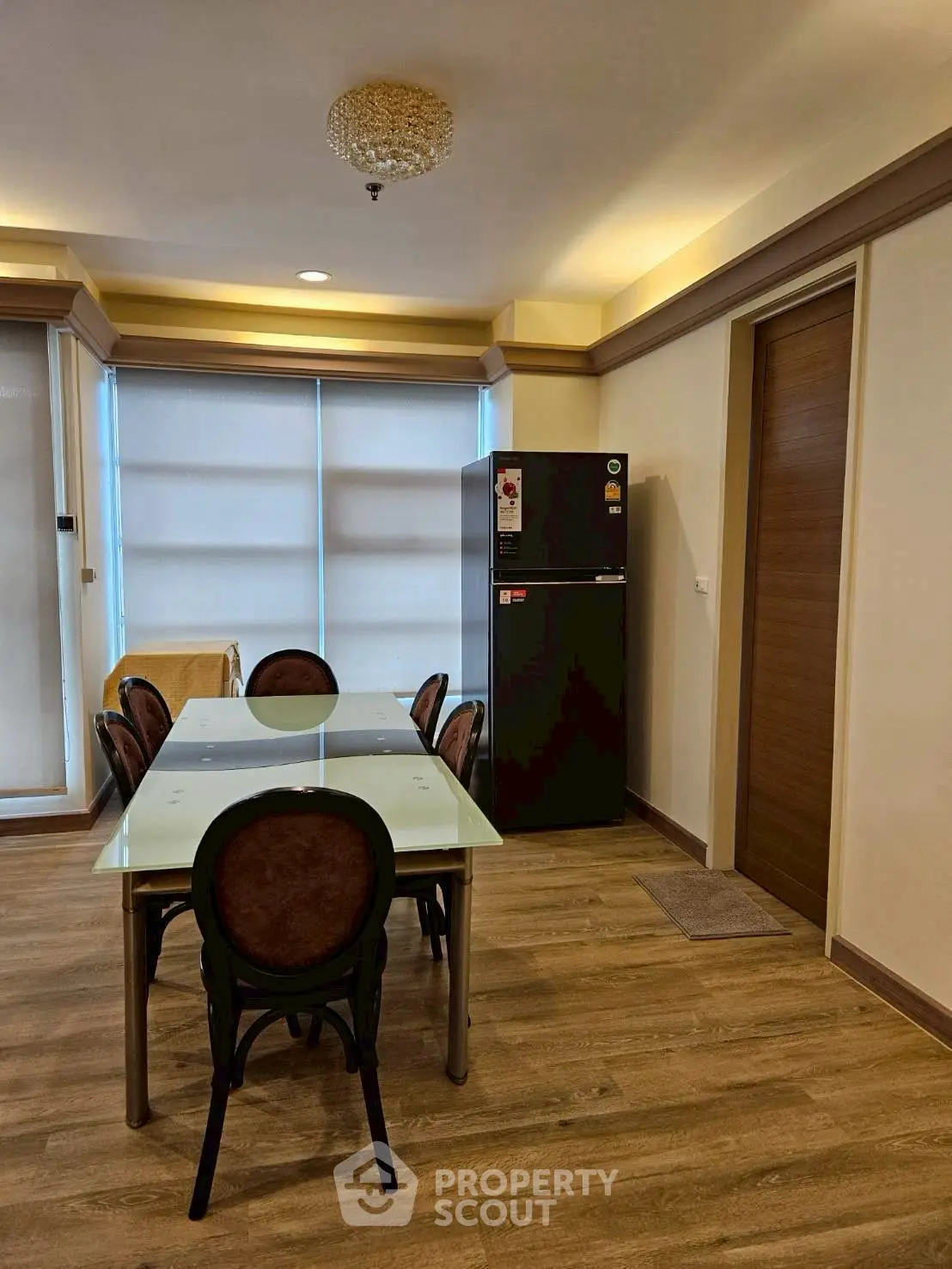 Modern dining area with glass table and elegant chairs, featuring a sleek refrigerator and wooden flooring.
