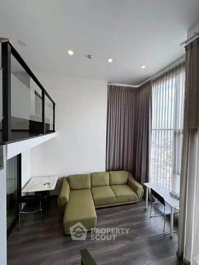 Modern loft-style living room with high ceilings and large windows offering city views.