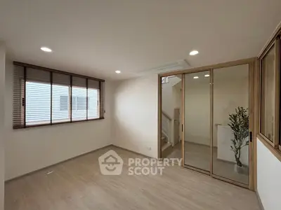 Spacious modern room with wooden flooring and large window, perfect for versatile living space.