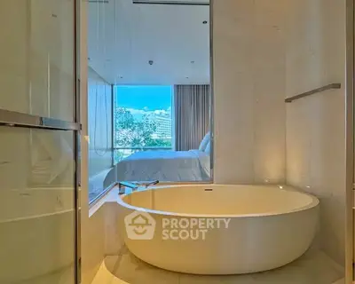 Luxurious bathroom with modern round bathtub and scenic view of bedroom and city skyline.