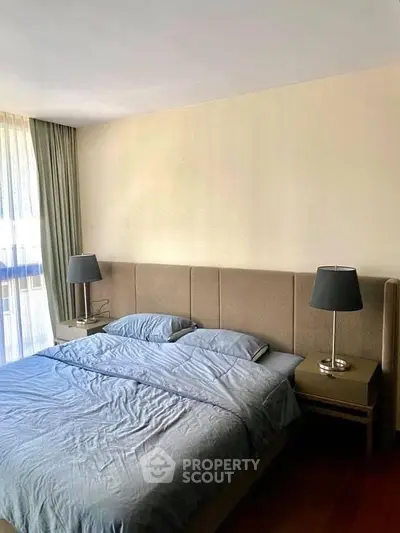 Spacious bedroom with elegant decor and natural light, featuring a comfortable bed and stylish lamps.