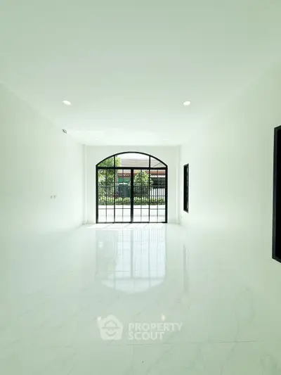 Spacious empty room with large arched window and marble flooring, perfect for customization.