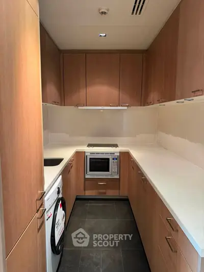 Modern kitchen with sleek wooden cabinets and built-in appliances, featuring a washing machine and microwave.