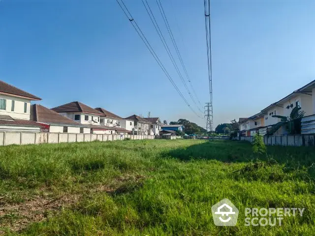 Expansive green field in a residential area with potential for development, under clear blue skies, surrounded by suburban homes.