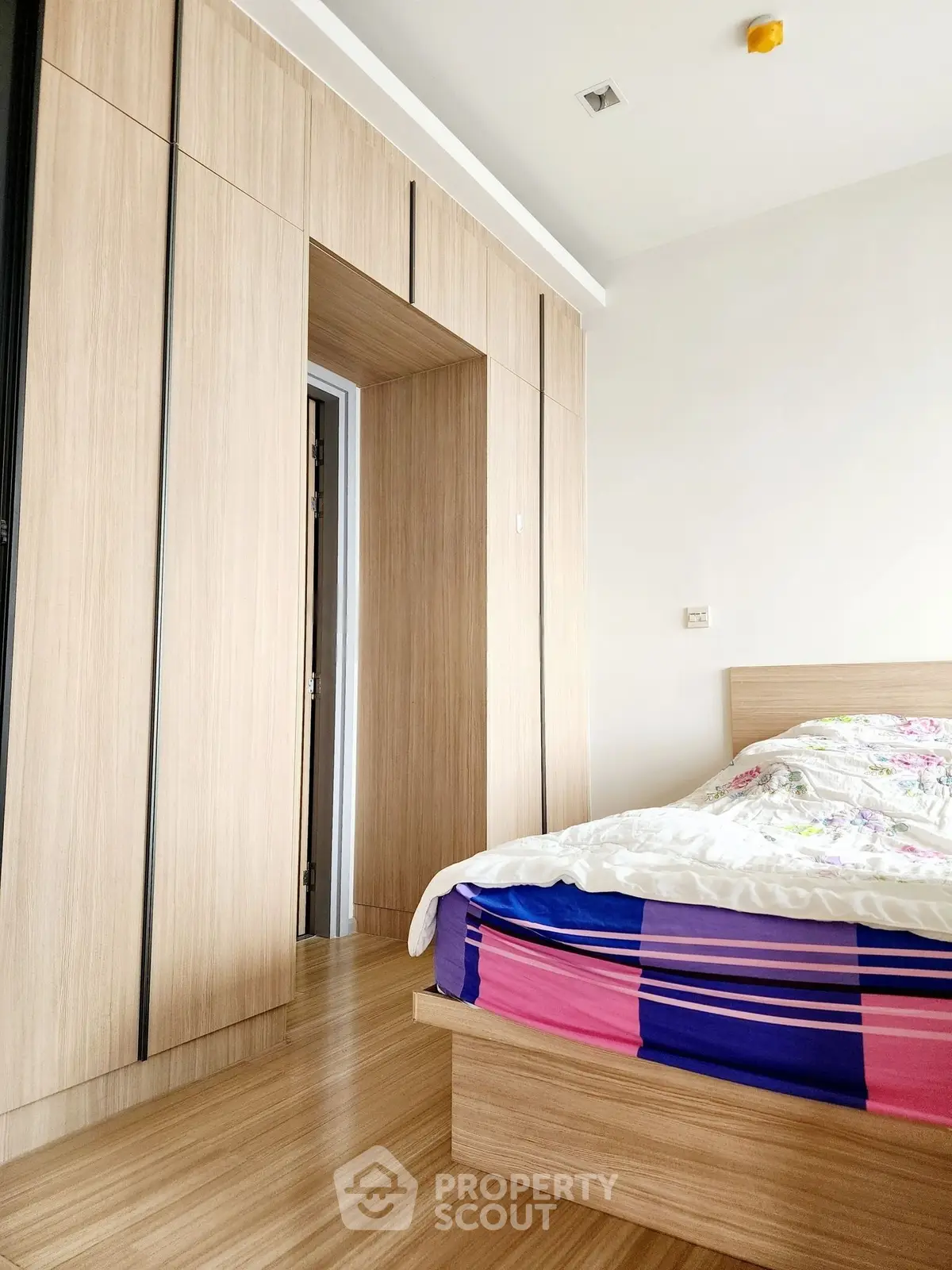 Modern bedroom with wooden flooring and built-in wardrobe, featuring a cozy bed with colorful bedding.