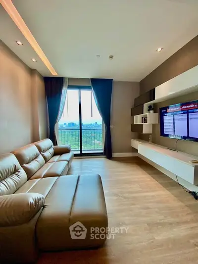 Modern living room with leather sofa and city view from balcony, featuring sleek wall-mounted TV unit.