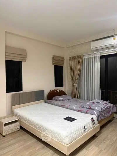 Spacious bedroom with twin beds and modern decor, featuring large windows and air conditioning.