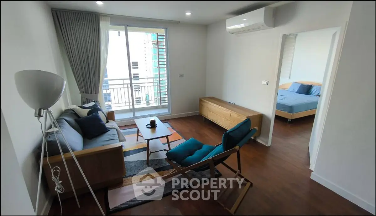 Modern living room with wooden flooring and stylish furniture, featuring a cozy seating area and a glimpse of the bedroom.