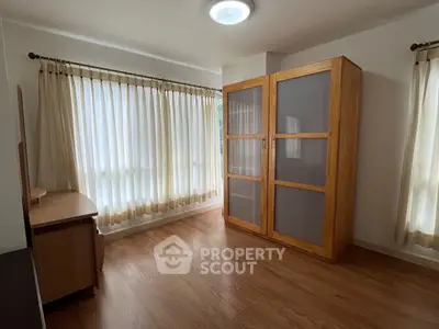 Spacious bedroom with wooden flooring and large windows for natural light.