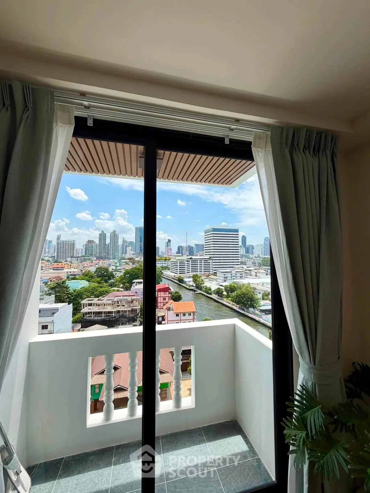 Stunning city view from a modern apartment balcony with sliding glass doors and lush curtains.